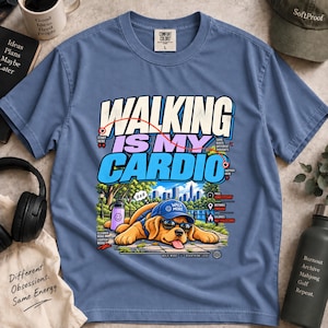 May include: A blue short-sleeve t-shirt featuring a graphic of a golden retriever wearing a blue cap and sunglasses, lying down. The text reads "WALKING IS MY CARDIO" with additional small labels including "PACE UNNECESSARY" and "DISTANCE ENOUGH".