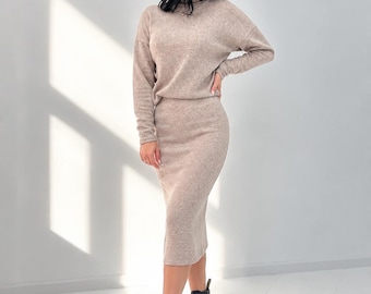 May include: A beige two-piece set consisting of a long-sleeved mock neck sweater and a matching midi-length skirt, paired with black lace-up combat boots. The fabric has a soft, heathered texture throughout the top and the skirt.