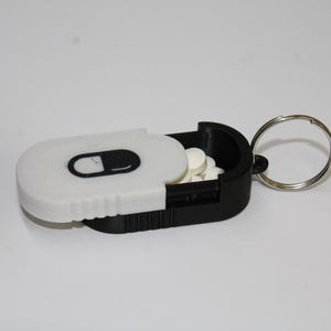Estuche compacto para pastillas con tapa deslizante, ideal para vitaminas y objetos pequeños de viaje.