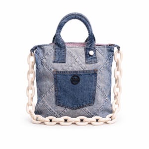 Può includere: Una borsa tote in denim azzurro lavaggio acido con motivo trapuntato a rombi, due manici superiori e una spessa tracolla a catena in plastica color bianco sporco. Una tasca in denim blu scuro è centrata sul davanti con una toppa logo.