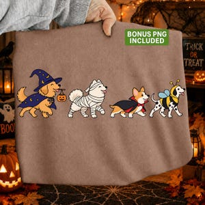 May include: A brown sweatshirt featuring a graphic of four dogs in Halloween costumes: a golden retriever as a wizard with a pumpkin bucket, a white dog as a mummy, a corgi as a vampire, and a dalmatian as a bumblebee. Text reads BONUS PNG INCLUDED.