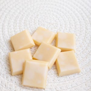 Pode incluir: Oito pastilhas de cera quadradas, amarelo claro, dispostas sobre uma superf&iacute;cie branca texturizada. As pastilhas de cera t&ecirc;m um aspeto liso e brilhante. O conjunto sugere um produto de ambienta&ccedil;&atilde;o para a casa, possivelmente para um queimador de &oacute;leos. O aspeto &eacute; simples.
