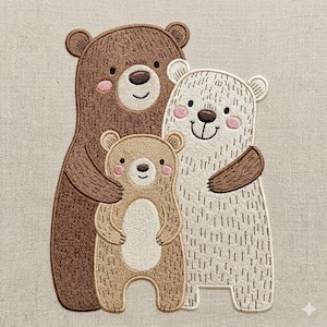 Puede incluir: Imagen bordada de una familia de osos. La imagen presenta tres osos: un gran oso marrón, un oso beige más pequeño y un oso blanco. Los tres osos se abrazan. Los osos tienen mejillas rosadas y caras sonrientes. El fondo es de color beige claro.
