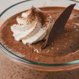 Peut inclure: Gros plan sur un dessert au chocolat dans un verre transparent. Le dessert est garni de crème fouettée et de cacao en poudre, ainsi que d'un copeau de chocolat noir. Le dessert est d'une riche couleur marron.