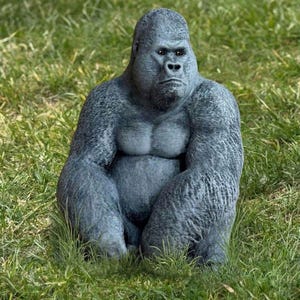 May include: A gray gorilla statue with a stern expression sits in green grass. The gorilla has a muscular build and detailed fur texture. The statue is a decorative garden ornament.