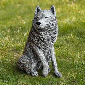 May include: A gray wolf statue with detailed fur texture, sitting upright on green grass. The statue has a realistic appearance with a focused gaze and a dark nose. The outdoor garden decor piece is made of a durable material.