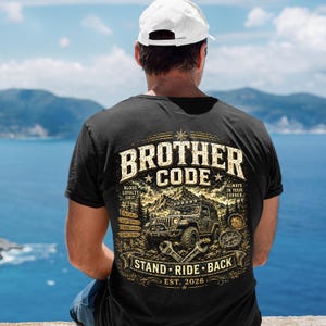 Puede incluir: Una camiseta negra de manga corta con un gráfico en la espalda que incluye el texto BROTHER CODE, STAND RIDE BACK y EST. 2026. El diseño muestra un vehículo todoterreno, montañas, llaves inglesas y una brújula, con las palabras BLOOD, LOYALTY, GRIT.