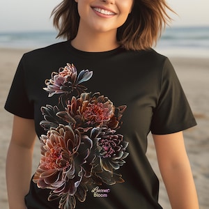 Op de afbeelding: Zwart T-shirt met een bloemenontwerp in rood-, bruin- en paarse tinten. De afbeelding bevat de tekst "Lucent Bloom". De bloemen hebben gedetailleerde, ingewikkelde lijnen.