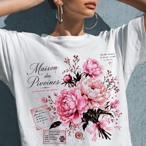 May include: A white t-shirt featuring a graphic print of pink peony flowers, a small pink ribbon, and French text that reads Maison des Pivoines, collection du matin, and other smaller script details. The design includes a rectangular paper-like element.