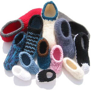 Op de afbeelding: Een verzameling gebreide pantoffels in verschillende kleuren, waaronder rood, blauw, zwart en wit. De pantoffels hebben verschillende patronen en afwerkingsdetails, die een handgemaakte uitstraling laten zien. Sommige hebben gestreepte of getextureerde ontwerpen.
