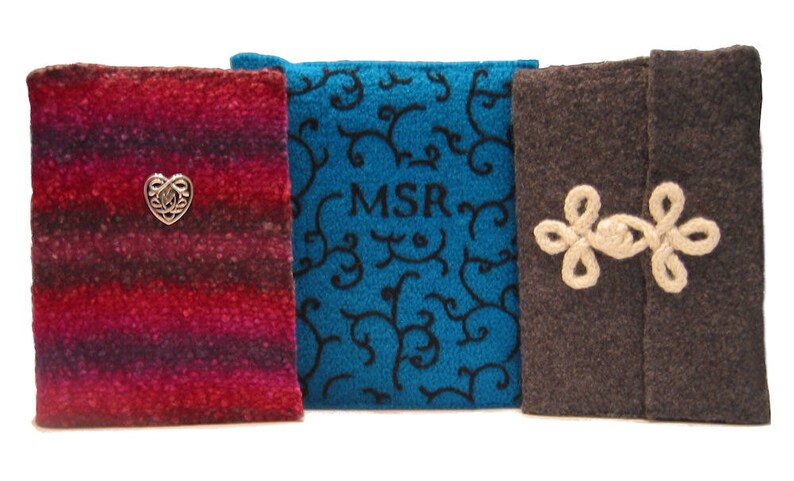 Op de afbeelding: Drie stoffen boekomslagen in rood, blauwgroen en bruin. De rode omslag heeft een zilveren hartvormige versiering. De blauwgroene omslag heeft zwarte krullen en de initialen "MSR". De bruine omslag heeft een cr&egrave;mekleurige bloemensluiting.