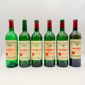 Op de afbeelding: Zes wijnflessen van donkergroen glas met rode foliecapsules op de halzen. Elke fles heeft een crèmekleurig etiket met de tekst PETRUS POMEROL GRAND VIN, een ronde portretillustratie en een rood embleem met een witte letter P.