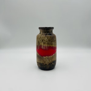 Puede incluir: Un jarrón de cerámica vintage con un acabado texturizado marrón y beige y una audaz franja horizontal roja. El jarrón tiene un borde y una base de color marrón oscuro, y una forma cilíndrica, adecuado para la decoración del hogar.