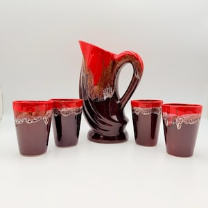 Puede incluir: Una jarra de cerámica y cuatro vasos a juego con una base de color burdeos intenso que se transforma en un esmalte rojo vibrante en la parte superior, con un efecto texturizado de goteo donde los colores se encuentran.