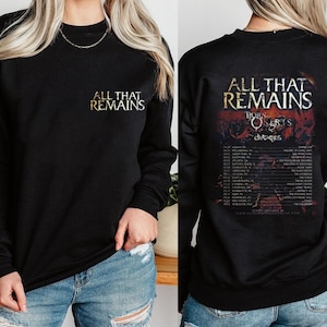 Könnte beinhalten: Schwarzes Langarm-Sweatshirt mit goldenem Text "ALL THAT REMAINS" auf der Vorderseite. Auf der Rückseite befindet sich eine Tourgrafik mit dem Bandnamen "BORN OF OSIRIS" und Tourdaten. Ein Konzert-Merchandise-Artikel.