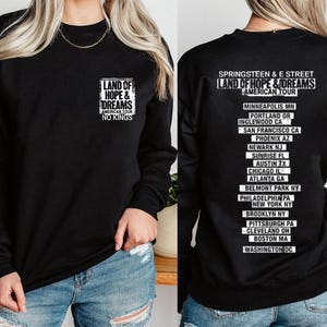 May include: Black long-sleeve sweatshirt featuring the text "LAND OF HOPE & DREAMS AMERICAN TOUR NO KINGS" on the front. The back of the sweatshirt lists tour cities including Minneapolis, Phoenix, and New York.