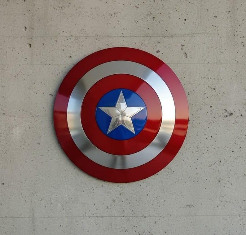 May include: A round shield with a red outer ring, a silver inner ring, and a blue center. A silver five-pointed star is in the center. The shield is mounted on a gray concrete wall.