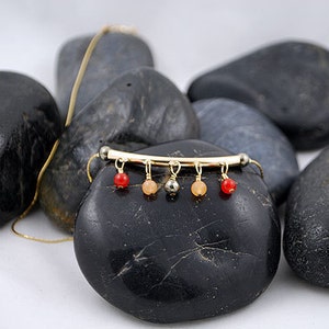 May include: A gold necklace with a bar pendant and dangling red, orange, and gray beads.