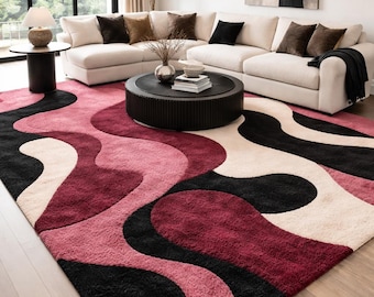 May include: A large rectangular area rug featuring a high-pile texture with a bold, abstract pattern of flowing, wavy bands in shades of deep burgundy, soft pink, cream, and solid black, covering the floor in a living room setting.