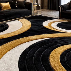 Pode incluir: Um tapete grande com um padr&atilde;o geom&eacute;trico arrojado de c&iacute;rculos conc&ecirc;ntricos em preto, branco e dourado. O design utiliza uma textura de pelo alto e baixo para criar profundidade, com faixas circulares douradas e brancas sobre uma base preta.
