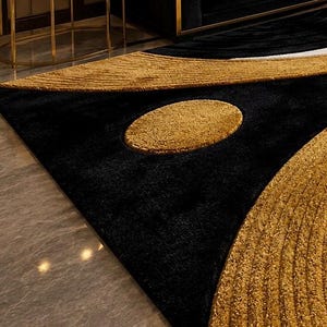 Pode incluir: Um tapete de pel&uacute;cia com um fundo preto profundo e padr&otilde;es texturizados em dourado contrastante. O design inclui uma forma oval dourada central proeminente e sec&ccedil;&otilde;es douradas curvas com uma textura de superf&iacute;cie nervurada em relevo.