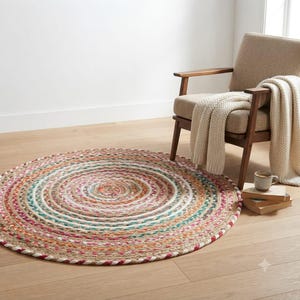 May include: A round, braided area rug featuring concentric circles of natural jute fiber interspersed with vibrant threads in shades of pink, teal, orange, and white. The rug has a textured, woven construction with a multi-colored, circular pattern.