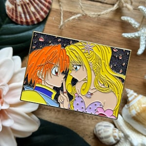 Könnte beinhalten: Rechteckiger Emaille-Pin mit goldenem Rand, der zwei Anime-Charaktere in einer romantischen Umarmung zeigt. Der Mann hat orangefarbenes Haar, die Frau blondes Haar, vor einem sternenklaren Hintergrund.