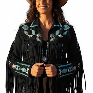 Könnte beinhalten: Schwarze Fransenjacke mit türkisen und silbernen Verzierungen. Die Jacke hat dekorative Nähte und Fransen an den Ärmeln und am Saum. Ein brauner Cowboyhut und türkisfarbener Schmuck vervollständigen den Western-Look.
