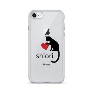 以下が含まれることがあります： 黒い猫が赤いハートを持っているデザインの透明なiPhoneケース。「shiori」という名前が猫の下に黒で印刷され、その下に「iPhone」と書かれています。透明なデザインです。