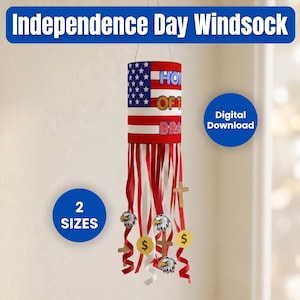 May include: A cylindrical Independence Day windsock featuring the American flag pattern with the text Home of the Brave. It has red and white streamers decorated with eagle illustrations, wooden cross shapes, and yellow circular coin-like accents.