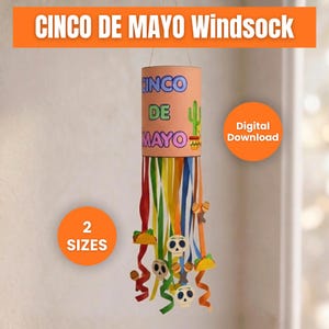 Puede incluir: Un molinete de Cinco de Mayo con serpentinas coloridas y elementos decorativos. El cuerpo cilíndrico presenta texto y una ilustración de cactus. El diseño incluye calaveras colgantes, tacos y maracas.