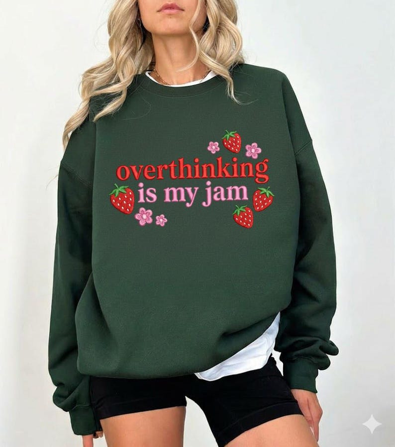 May include: Dark green sweatshirt with the phrase "overthinking is my jam" in red and pink lettering. The design includes strawberry and flower graphics. The sweatshirt is a casual style.