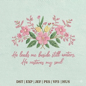 以下が含まれることがあります： ピンクの花、黄色のアクセント、緑の葉が特徴の刺繍された花の模様。「He leads me beside still waters. He restores my soul」というテキストが筆記体で書かれています。背景は水色のテクスチャパターンです。
