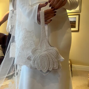 Ivory evening bag held in hands, featuring an oversized hand‑beaded floral design made of pearl‑style beads.
