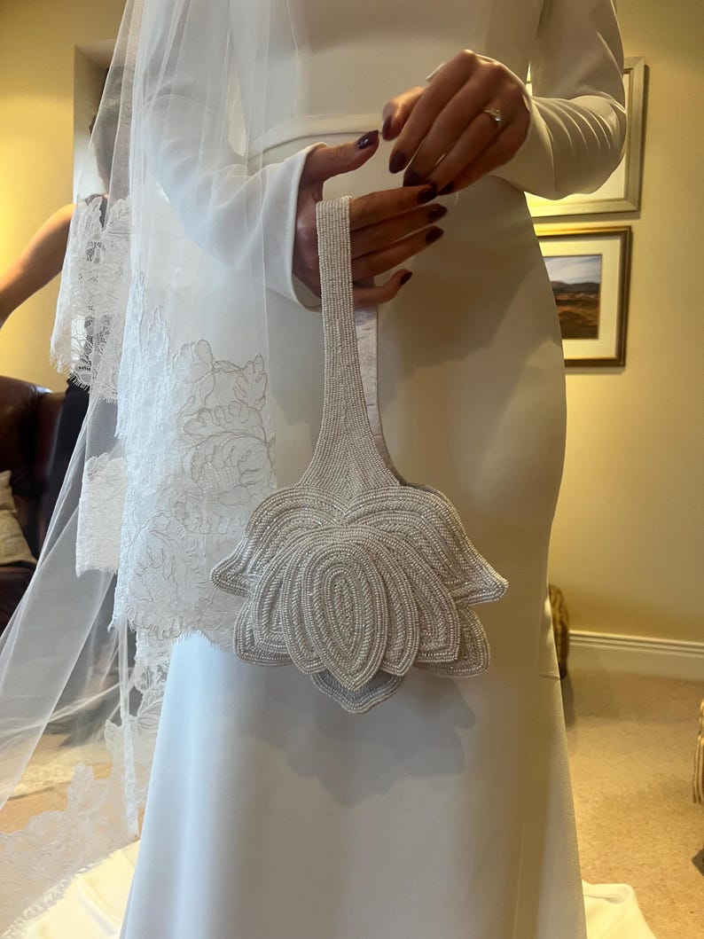 Ivory evening bag held in hands, featuring an oversized hand‑beaded floral design made of pearl‑style beads.
