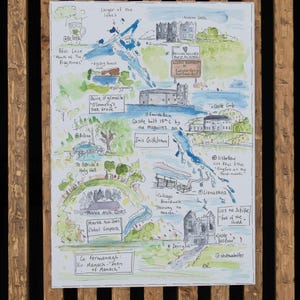 May include: A hand-drawn watercolor map of Enniskillen, Ireland, highlighting local landmarks and points of interest. The map features a blue and green color scheme with handwritten text and illustrations. Some of the landmarks include: Marble Arch Caves, St. Patrick's Holy Well, Castle Coole, and Lios na Scéithe.