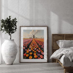 Puede incluir: Una impresión enmarcada representa un campo de tulipanes de colores que conduce a un molino de viento bajo un cielo nublado. La obra de arte se exhibe en una habitación con una paleta de colores neutros, junto a una planta en maceta y una cama con marco de madera.