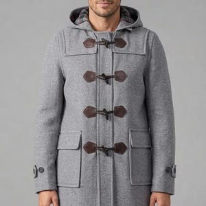 以下が含まれることがあります： フードと茶色のトグル留めが付いたグレーのダッフルコート。 コートには2つのフロントポケットがあり、フードにはチェック柄の裏地が見えます。 コートはウール混紡で作られています。