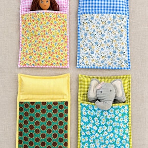 Peut inclure: Quatre sacs de couchage rectangulaires en tissu pour petites poupées ou peluches. Chacun présente une section oreiller à carreaux vichy et une section couette à motifs floraux ou tournesols. L'un contient une poupée brune et l'autre un éléphant.