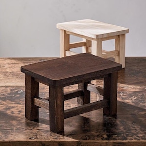 May include: Two small wooden stools, one with a dark brown finish and one with a natural light wood finish. Each stool features a rectangular top supported by four sturdy legs connected by horizontal crossbars on all four sides of the base.