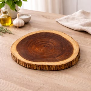 May include: A round wooden chopping board with a natural edge. The board is made of dark brown wood with a lighter brown edge. The wood grain is visible. The board is approximately 30 cm in diameter.