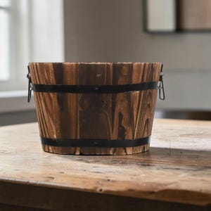 May include: A round wooden bucket featuring a dark brown stained finish with visible wood grain patterns. The bucket is reinforced with two horizontal black metal bands and includes two black metal side handles attached to the upper rim.