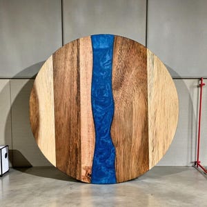 Puede incluir: Tabla redonda de madera para servir con diseño de río de resina azul. La tabla está hecha de varios tonos de madera, con un río central de resina azul brillante. Aproximadamente 46 cm de diámetro.