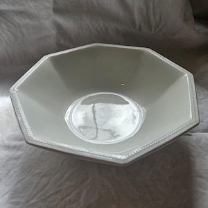 May include: A white octagonal bowl with a smooth, glossy finish and a decorative beaded border along the rim. The bowl features eight distinct sides that slope inward towards a circular base, creating a clean and symmetrical geometric design.