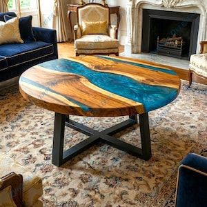 Puede incluir: Mesa de centro redonda de madera con un diseño de río de resina azul. La mesa tiene una veta de madera marrón oscuro y una base de metal negro. Un mueble único para un salón.