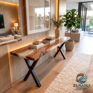 May include: A console table featuring a live-edge wood slab with a central white resin inlay, supported by black metal X-shaped legs. The table holds two stacks of books, each topped with a ceramic bowl, and a tall vase with greenery.