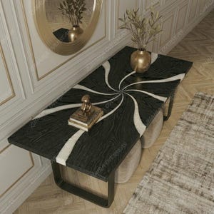 May include: A rectangular black wooden table with a white swirl design. The table has a black metal frame and is decorated with a gold vase, a small gold statue, and a stack of books. The table is 152 cm long and 76 cm wide.