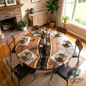 Puede incluir: Una mesa de comedor redonda de madera con una incrustación central de resina negra rellena de piedras de río lisas. La mesa está dispuesta con seis cubiertos, cada uno con un plato blanco, un cuenco y una servilleta. Seis sillas con asientos tapizados en gris oscuro rodean la mesa.