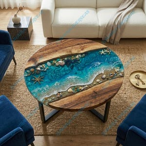 May include: Round wooden coffee table with a unique ocean-themed design. The table features a central resin inlay with seashells, pebbles, and starfish, mimicking a beach scene. The table has a dark metal base and is surrounded by blue chairs.