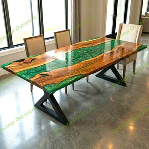 May include: A rectangular wooden dining table with a green epoxy resin center. The table has a natural wood grain pattern with a glossy finish. The base is made of black metal and has an X-shaped design. The table is approximately 96 inches long.